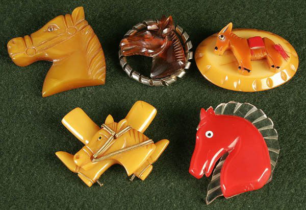 5 CARVED BAKELITE HORSEHEAD PINS first half of th: 5 CARVED BAKELITE HORSEHEAD PINS first half of the 20th century, comprising caramel, root beer and French red with Lucite mane. 2"-2.5". Estimate $150-$250