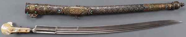 A UNIQUE & ORNATE SILVER MOUNTED OTTOMAN YATAGAN: A UNIQUE AND ORNATE SILVER MOUNTED OTTOMAN YATAGAN, CIRCA 1890. The recurved single edged blade with double fuller and grooved spine and flared tang with chased decoration and set with paste stones a