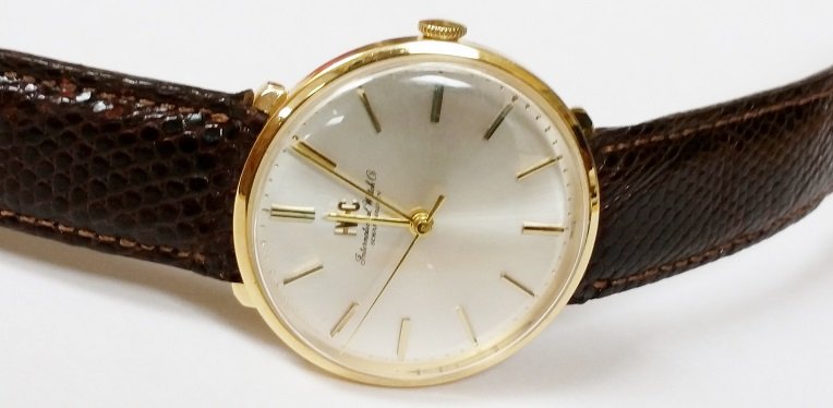vintage IWC 18K Yellow Gold watch: A 1962 vintage IWC 18K Yellow Gold watch with a unique, recessed strap design and a silver/grey dial with applied gold bar markers.