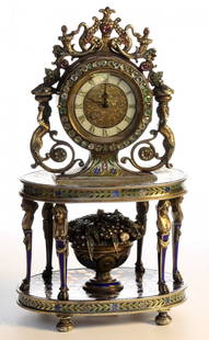 A silver and enamel gem set clock ,.Vienna c1875: A silver & enamel gem set clock,the clock sits on a miniature table, the legs in the form of ladies, on the base of the table is a basket of flowers set with pearls , rubies & emeralds. Vienna c1875