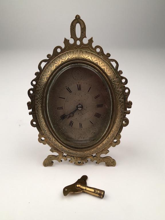 A strutt clock after those of Thomas Cole with a silver: A strutt clock after those of Thomas Cole with a silver facehand dial with painted Roman numerals.The oval case is with a pierced brassfront and a easle back.4 inches wide x 5 inches high.