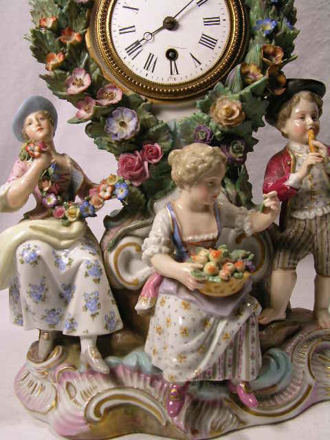 PORCELAIN MANTEL CLOCK WITH FOUR FIGURINES. CHIP