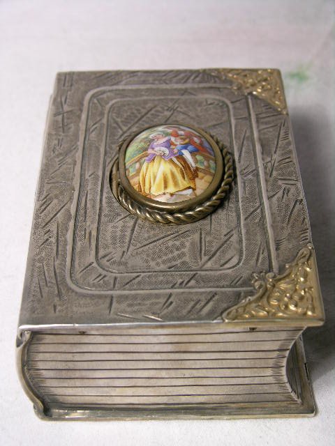 MECHANICAL SINGING BIRD BOX.: STERLING SILVER MECHANICAL SINGING BIR BOX IN THE FORM OF A BOOK. THE COVER IS OF OF MAN PLAYING MUSIC TO A WOMAN. WHEN THE LID OPENS THE BIRD SINGS. STAMPED 925 SILVER. HEIGHT 1 1/2" LENGTH 5". DEPTH