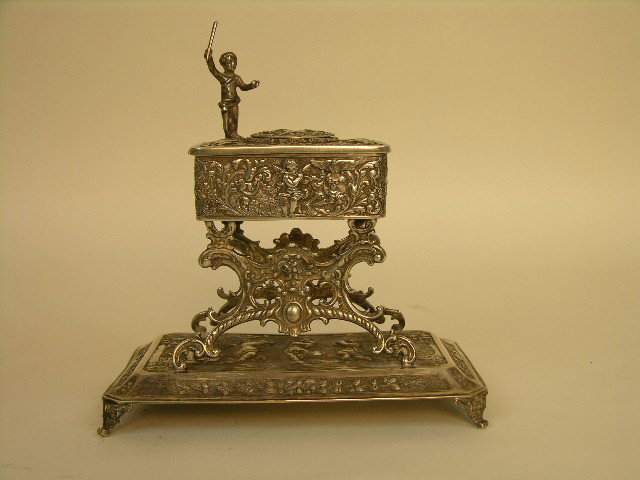 STERLING SILVER MECHANICAL SINGING BIRD BOX.: A STERLING SILVER MECHANICAL SINGING BIRD BOX. A MUSICAL CONDUCTOR STANDING ON THE TOP WITH HIS CONDUCTORS WAND, SUPPORTED ON FOUR SCROLLED FEET. WHEN THE SLIDE BAR IS SLID THE BIRD POPS UP AND SINGS 