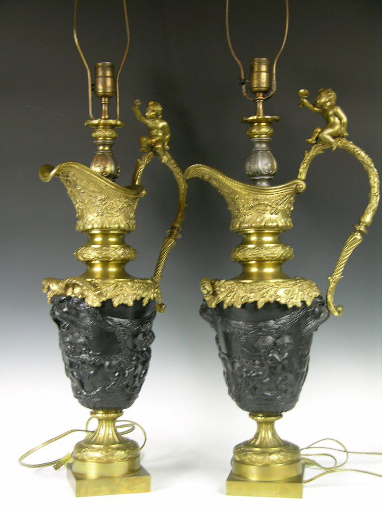 BRONZE TABLE LAMPS DECORATED WITH PUTTI ALL AROUND: A PAIR BRONZE TABLE LAMPS DECORATED WITH PUTTI ALL AROUND AND A ROARING LION ON EACH END, ONE LARGE HANDLE WITH A PUTTI ON TOP OF EACH HANDLE.OVERALL HEIGHT UP TO TOP OF HANDLE 26".ONE BASE STAMPED ON