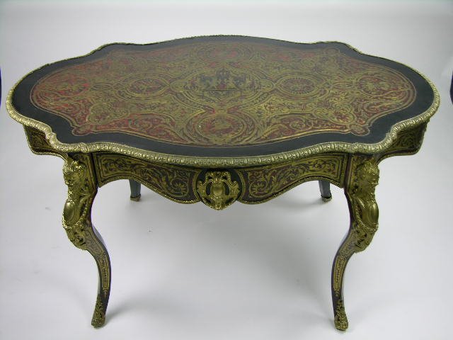 An ormolu mounted Boulle center table: An ormolu mounted Boulle center table, French last quarter 19th century. Of typical form with a shaped turtle top, red tortoiseshell inlaid with brass foliate strap work, trophies and figures, the fri