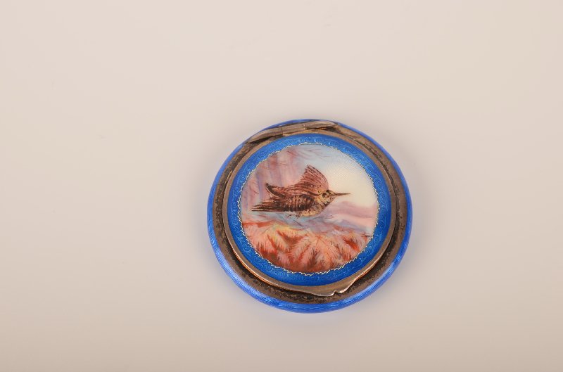 Guilloché enamelled round enamelled compact.: Guilloché enamelled round enamelled compact. A very well painted Humingbird in flight with a landscape in the background. Diameter 1 3/4".