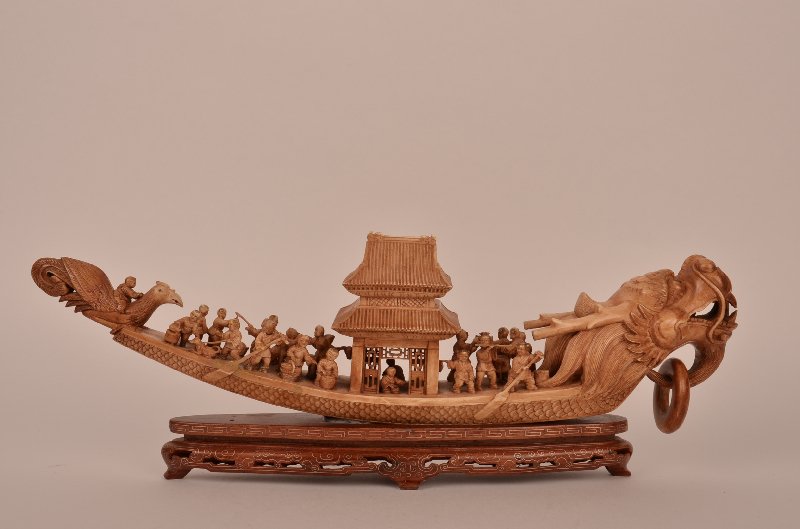 Carved Chinese ivory boat with large Dragon head: Carved Chinese ivory boat with large Dragon head on the bow and a large bird on the back, twenty two riders on-board, all mounted on a carved wood base. Length 14 3/4".