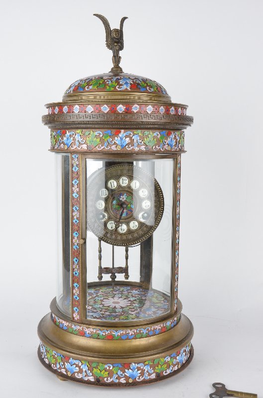 French Champleve clock with a figural finial.: French Champleve clock with a figural finial.four panels of curved and beveled glass.Overall height 21 inches.The back glass has been cracked. Mercury tubes missing.