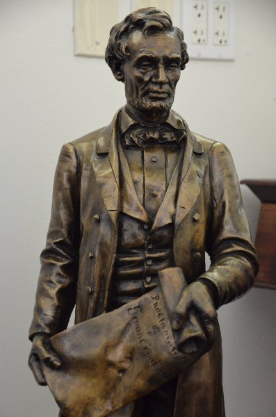 A bronze sculpture of a standing President Abraham: A bronze sculpture of a standing President Abraham Lincoln holding in his hands the Emancipation Proclamation. President Lincoln is dressed in formal attire with a slightly bowed head. The bronze is s