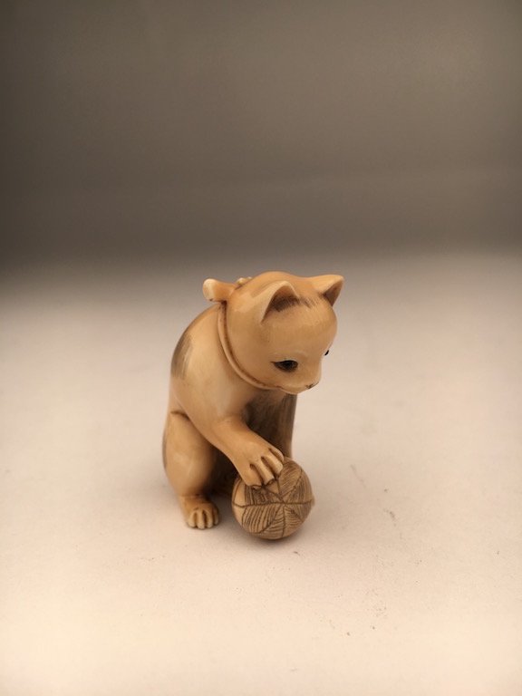 Carved Netsuke of a cat wearing a bow and playing with (1 of 4)