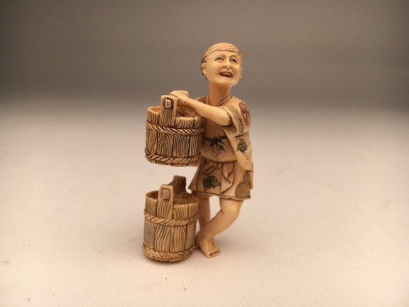 A carved Netsuke figure of a man carrying two buckets (1 of 3)