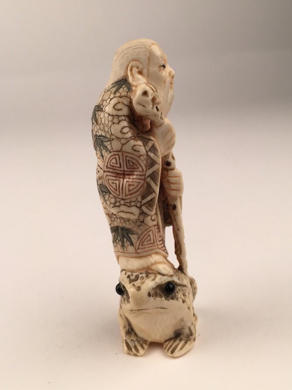 Carved Netsuke figure of an old man with a stick: Carved Netsuke figure of an old man with a stick standing on a frog.Height 2 5/8 inches.