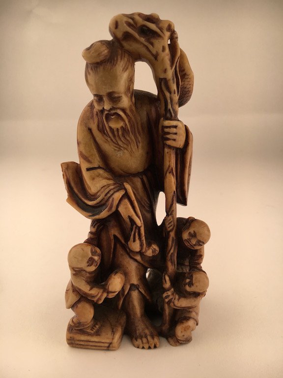 A carved soapstone figure of an old man holding a staff: A carved soapstone figure of an old man holding a staff with three young children playing. Height 6 inches.