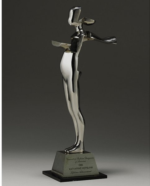 The Council of Fashion Designers of America Lifeti: The Council of Fashion Designers of America Lifetime Achievement Award, 1985 Steel statuette awarded to Katharine Hepburn, designed by the American artist Ernest Trova (b. 1929); together with a book
