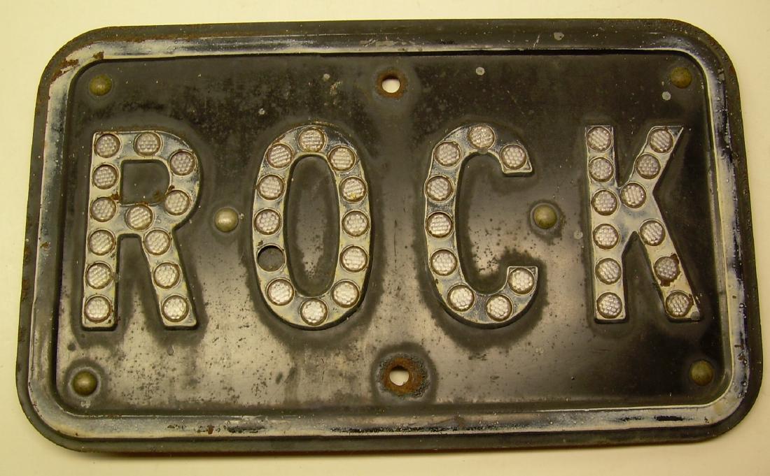 Sign ROCK with Cat's Eye Reflectors: A sign with cat's eye reflectors that has ROCK and a few mounting holes. It measures 15" by 9". It was on the Elmira to Sodus Point Branch of the P.R.R. in New York. It is a Block Limit sign; it has a