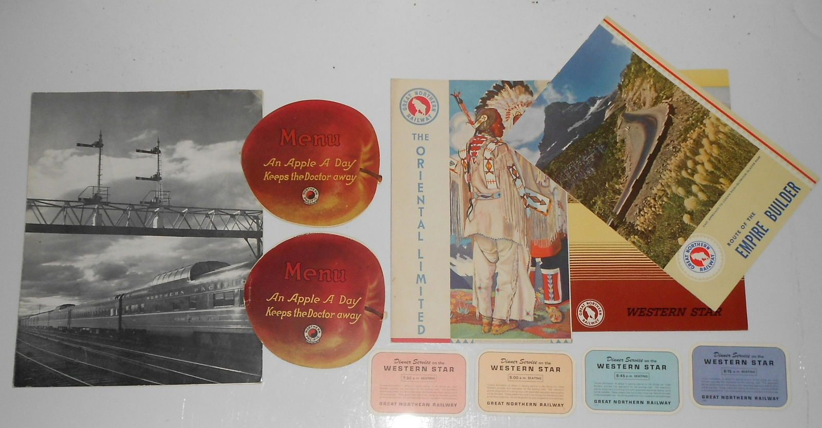 Railroad Dining Car Menus: GN NP: A group of 6 dining car menus & 4 diner invitation cards. 3 Northern Pacific Railway menus including 2 "apple" theme, 3 Great Northern & 4 small diner time cards from the Western Star, a GN name train