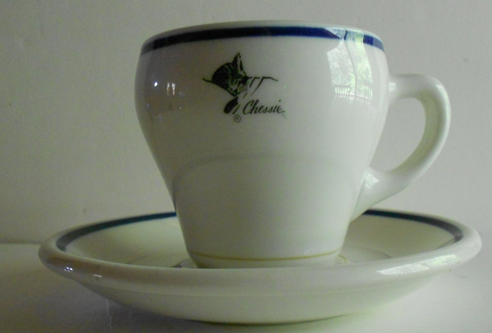 Chessie China Dolphin Cup & Saucer: A Chesapeake & Ohio Railway china cup and saucer set in the "Chessie" pattern. This unique cup style is called Dolphin after the inventor of the reverse curve top that would theoretically prevent spil