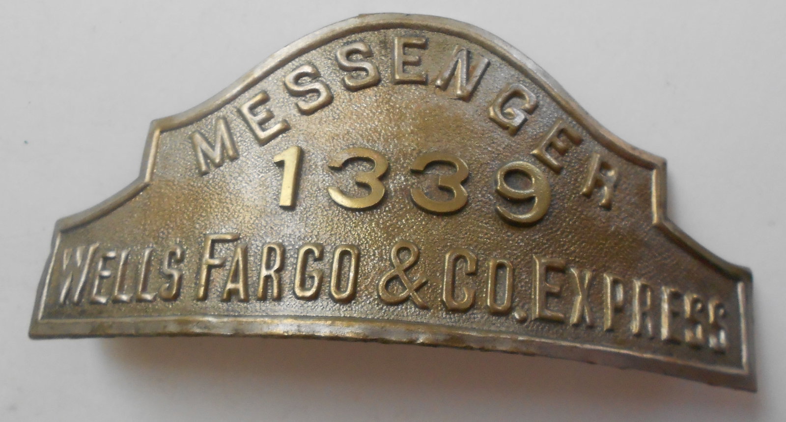 Wells Fargo Messenger Hat Badge - #1339: A hollow back dome shaped Wells Fargo & Company Express stamped across the bottom with applied numbers of 1339. Shows discoloration and 2 mounting tabs are present.