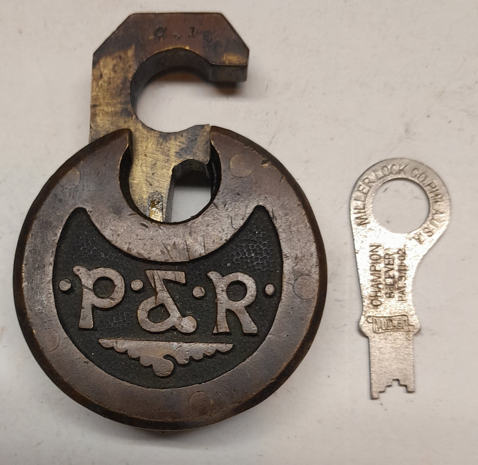 Philadelphia & Reading Brass Pancake Lock & Key: A brass push key lock with "P&R" heavily incised on one side. The shackle is stamped "C 1". It has an operating Miller key.