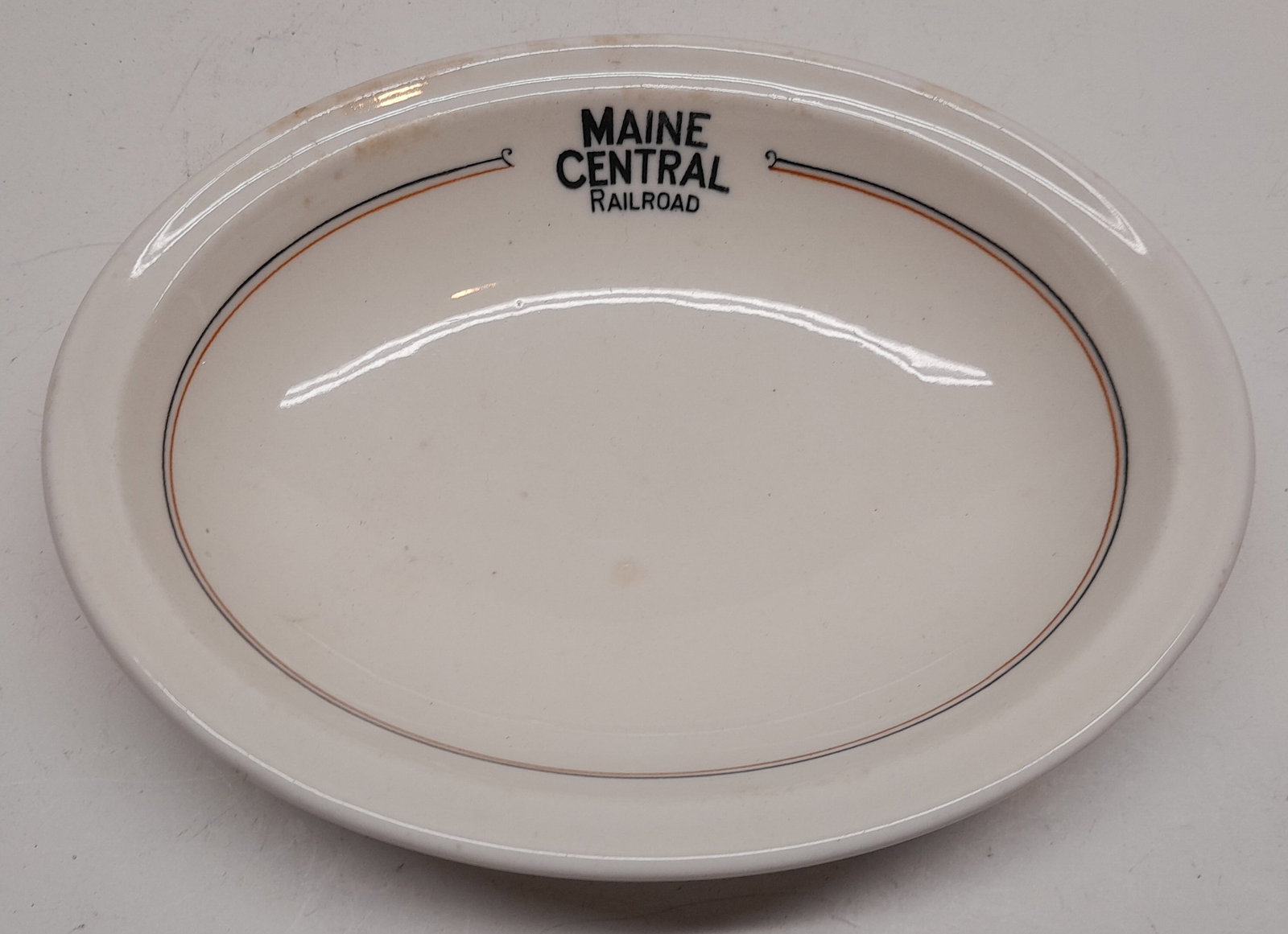 Maine Central Railroad "Kennebec" Pattern China Dish: Maine Central hard used "Kennebec" pattern oval dish with rimmed top. It has the standard Maine Central Railroad logo at 12:00 and 2 pinstripes. It has a Syracuse / OPCo standard hallmark with some ol