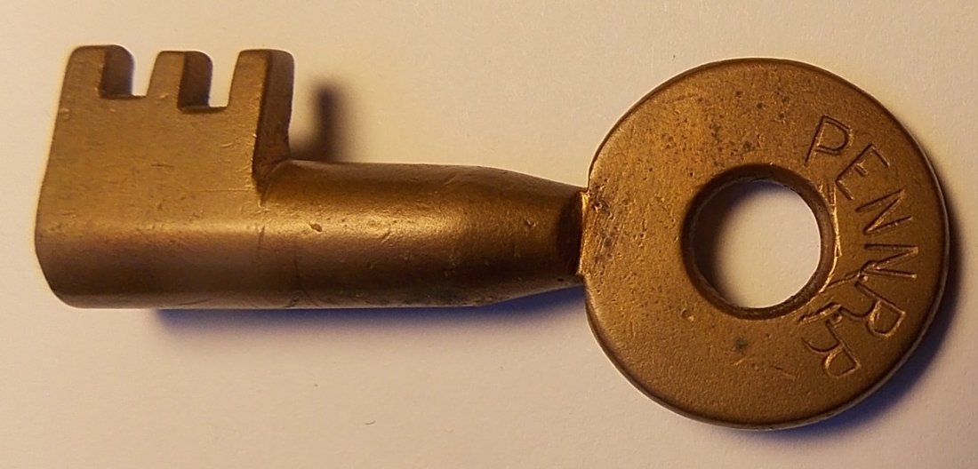 Pennsylvania Railroad J. L. Howard Brass Key: An early Pennsylvania Railroad key with a three parallel tooth bit. Fine "PENN RR" on the front and "J. L. Howard Hartford Conn" stamped on the reverse. Heavy taper to the barrel. No use. Some guys th