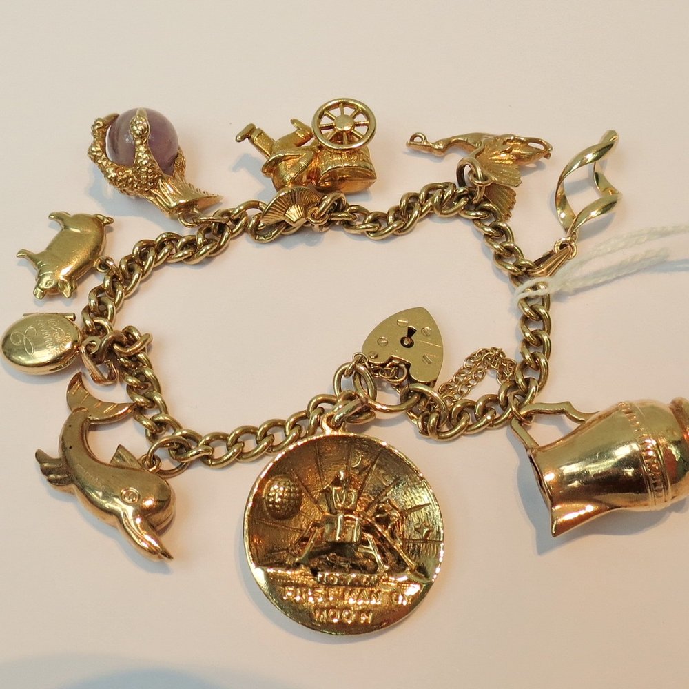 A 9ct gold charm bracelet, the curb link: A 9ct gold charm bracelet, the curb link chain fitted with a heart shaped lock and nine various charms including one commemorating the first moon landing, 32.24g.