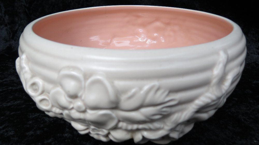 A Newport Pottery oatmeal and pink glazed bowl of: A Newport Pottery oatmeal and pink glazed bowl of ribbed form cast with flowers, varying ground, Clarice Cliff backstamp.