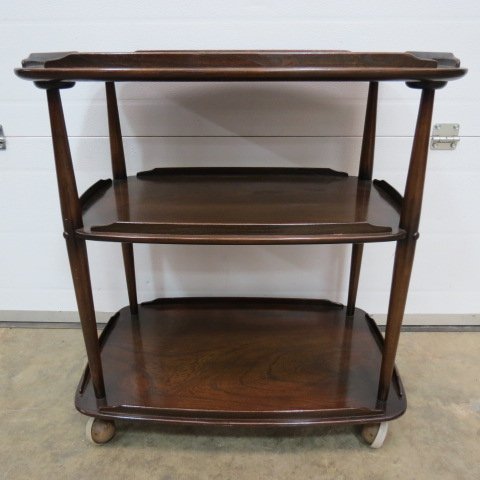 An Ercol oak three tier trolley, the rectangular: An Ercol oak three tier trolley, the rectangular shelves with a gallery between turned supports on shepherds castors. 71cm wide.