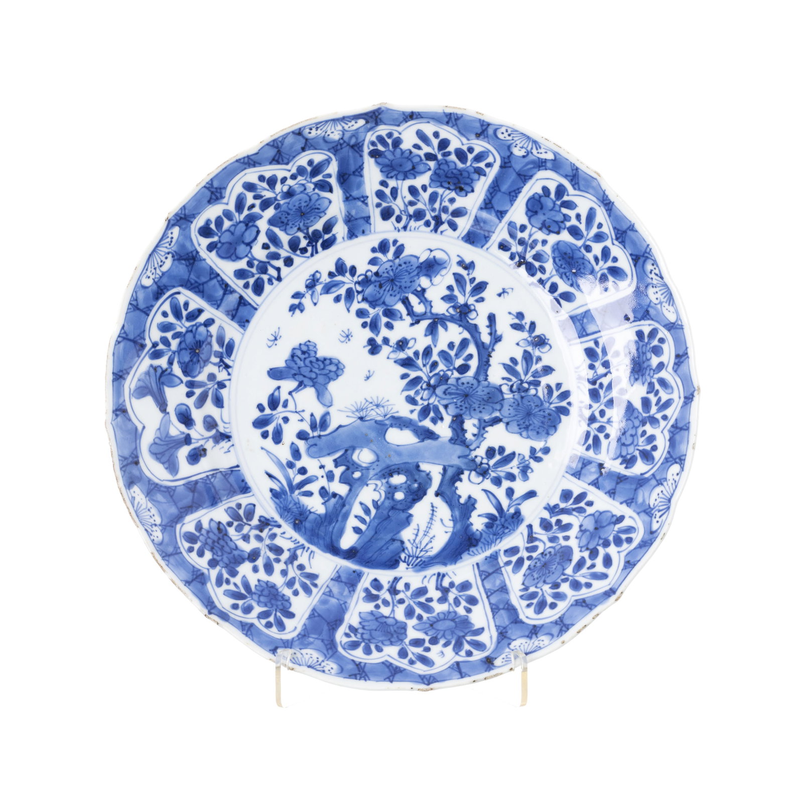 Plate with floral reserves in Chinese porcelain, Kangxi: China, Kangxi, blue and white decoration with floral reserves, scalloped brim, decorated back. Mark on base. Signs of use, minor nicks on the edge. Dim.:28cm.