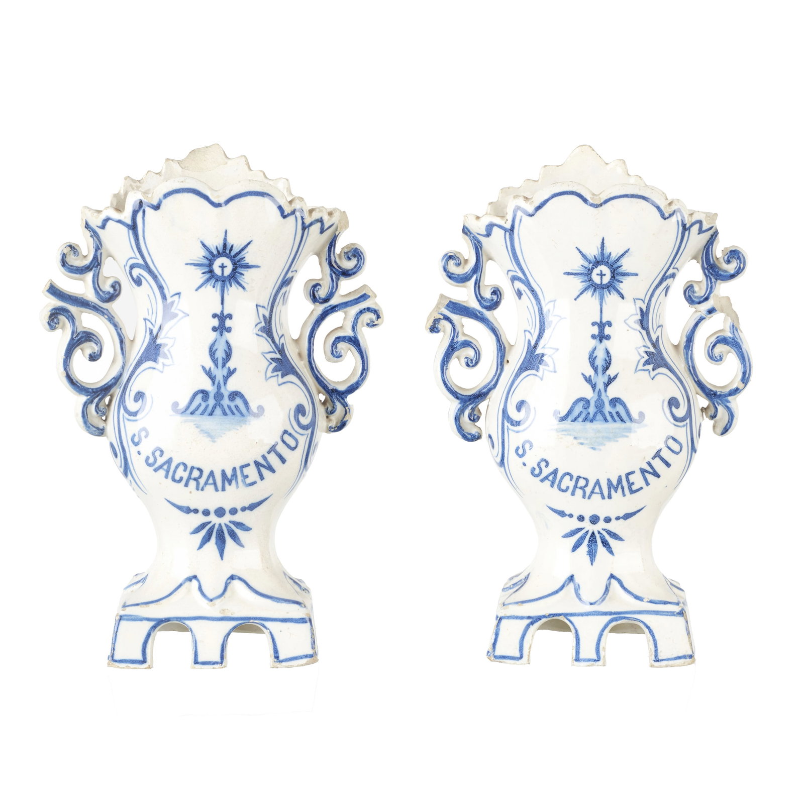 Pair of 'Holy Sacrament' jugs: Portuguese earthenware, 19th century, attributable to Massarelos, scalloped bodies with two openwork volute handles, resting on a scalloped front base; blue decoration with vegetal motifs and a