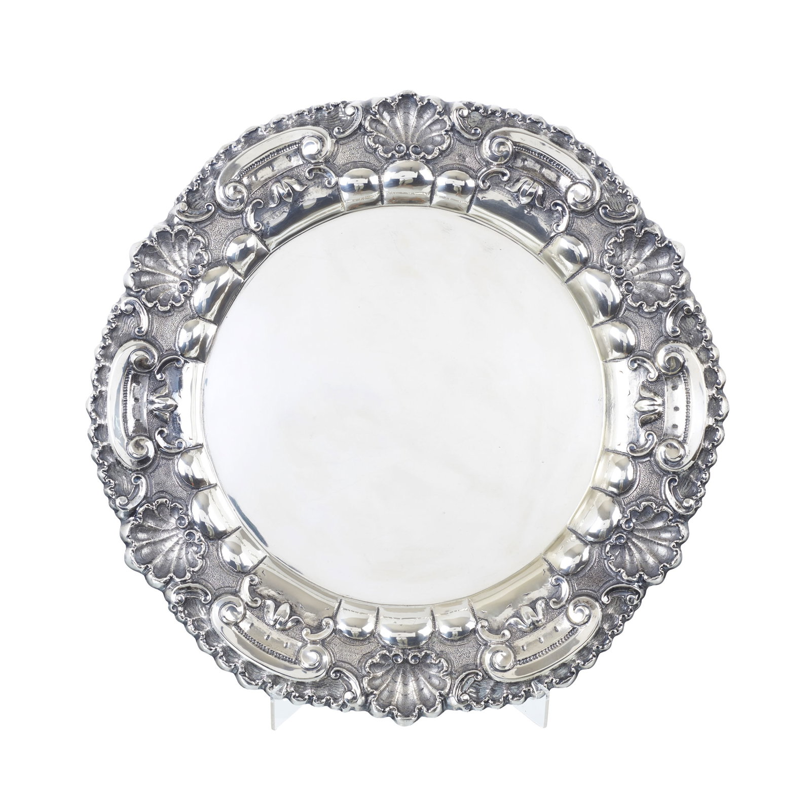 Large chased silver charger: Portuguese silver, 833 eagle hallmark (1938-1984), silversmith?s mark of Carlos Lago (reg. 1936); raised decoration of shells and scrolls. Signs of use. Approx. weight: 1500g. Dim.: 50.5cm.