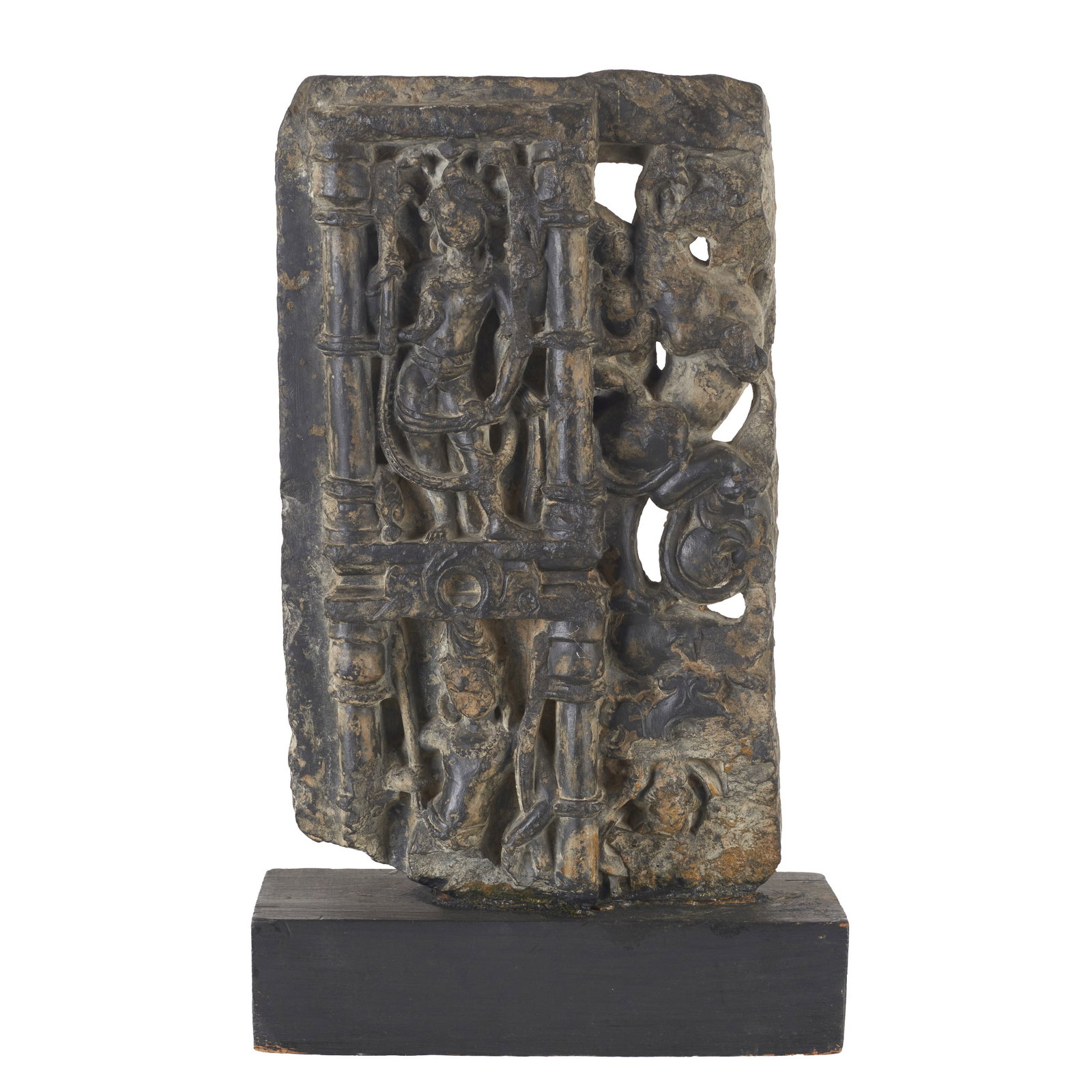 Hindu basalt plaque 'Indra': India, Rajasthan, 14th century, carved from basalt on a black wooden base, composition framed by Parikara, depicting Indra amongst other figures. Signs of use. Dim.: 34.5cm.