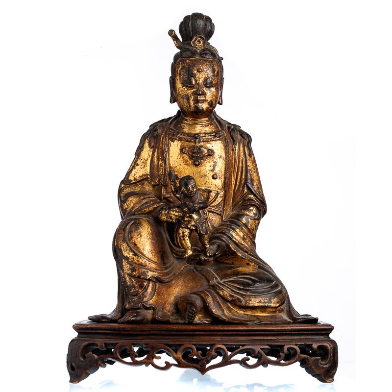 Chinese Guanyin in gilded bronze, Ming: Chinese sculpture in gilded bronze, Ming Dynasty (1368-1644), representing Guanyin in lotus position, holding a child, base in carved wood. Signs of wear. Dim.:32,5cm; with base: 38,5cm..