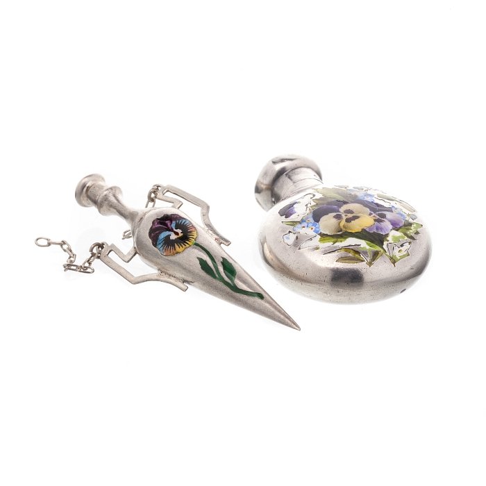 Two Art Nouveau perfume flasks in silver: Hanging amphora and round flask, one with London assay mark dated 1942, decorated with bouquet of pansies in enamel. Approx. weight:.:21,6grs. Dim.:6,7cm.