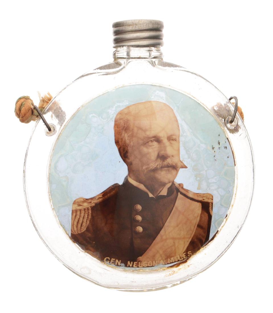 Gen. Nelson A. Miles Glass Canteen Flask.: Round glass flask with metal lid and braided rope. With a label under glass image of a General Nelson A. Miles. "U.S." is stamped on the back of the flask. Dimensions: 4-1/2"W x 5"T.