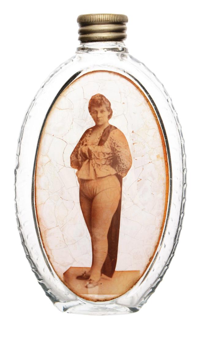Image Under Glass Flask.: Oval glass flask with diamond textured back and label under glass of a lady. The image displays crazing. Dimensions: 3-1/2"W x 6"T.