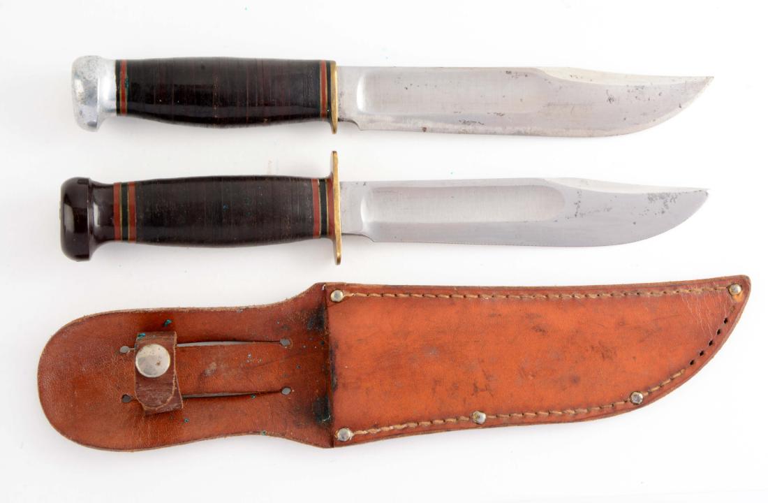 Lot of 2: Marbles Gladstone Mich. USA "Ideal" Fixed: Knife A) Clip point with fullers. Stacked leather handle, lignum vitae crown and full brass guard. Incorrect leather sheath. Circa post-1943. In very good condition. Knife B) Clip point with fullers.
