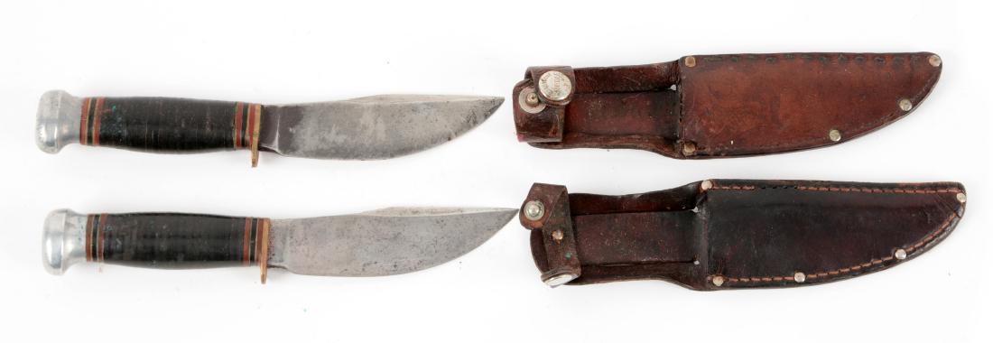 Lot of 2: Marbles Gladstone Mich. USA "Woodcraft": Knife A) Flat ground Skinner with thumb grooved back. Handled in stacked leather with aluminum crown and brass half guard. Correct leather sheath. Circa pre 1943. In very good condition. Knife B) Flat