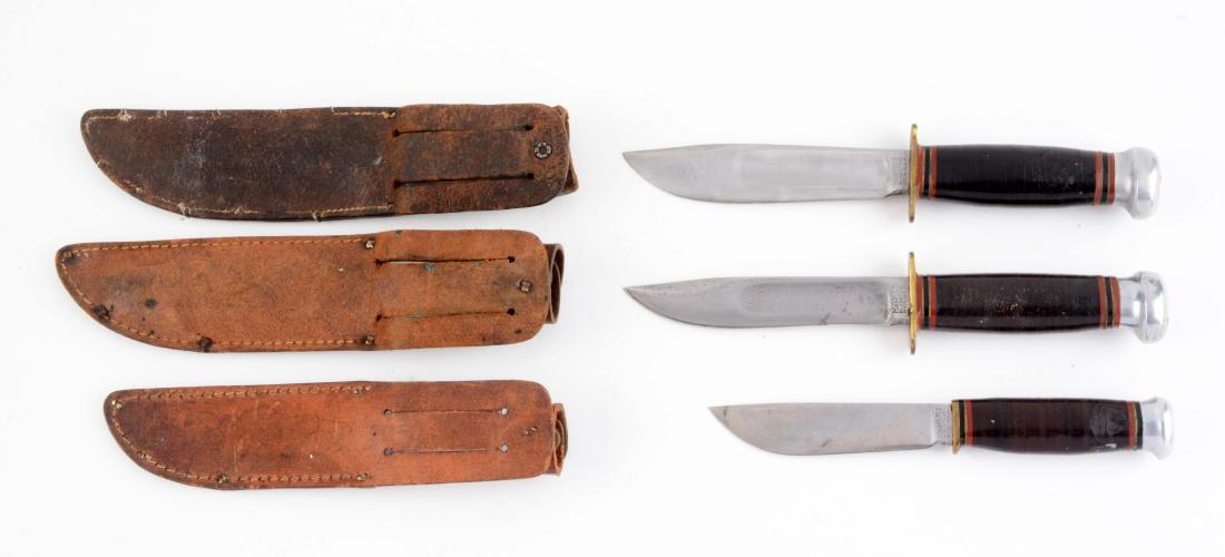 Lot of 3: Marbles Fixed Blade Knives.: Knife A) Sport Knife with a clip point blade. Stacked leather handle with aluminum crown and brass half guard. Correct Marbles leather sheath with signed safety snap and official Boy Scouts of America