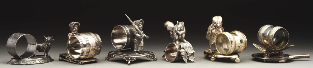 Lot of 6: Napkin Rings.: The first is a Kate Greenaway-type girl with rifle stands in front of napkin holder on footed, square base. By Simpson, Hall, Miller & Co. Silver and condition are very good. The second is a Kate Gree