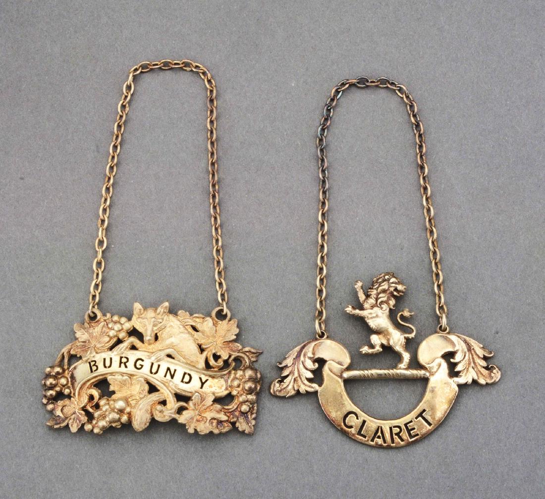 Two Boxed English Silver-Gilt Wine Labels.: Wyard-Druitt & Co., London 1970, the first cast as a crest of a lion rampant reguardant over a crescent banner with leafage ends pierced "CLARET"; the second cast as a cluster of fruiting vines around