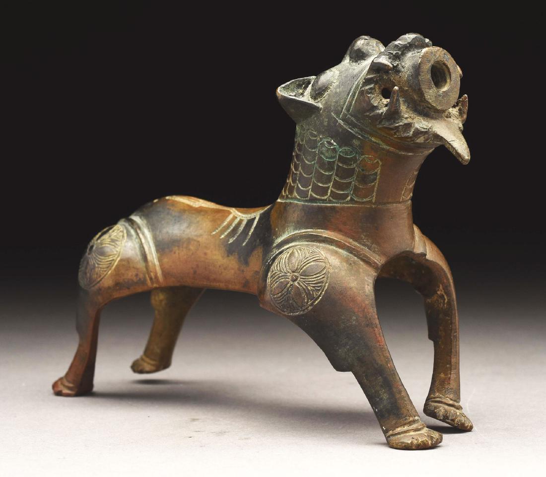 Bronze Aquamanile in the Form of a Dog.: 19th century or earlier. In the Asian taste, the guarding dog with opening for spout. Etched design of rondels and scales. Surface with good patina, a hole on each side of jaw of unknown purpose. Figu