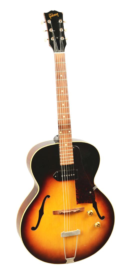 Gibson ES-125 Electric Guitar.: Hollow-body electric guitar with a dark sunburst finish, tortoise pickguard, and trapeze tail piece. Some crazing can be seen throughout the finish with scratches on the body and light splitting. With