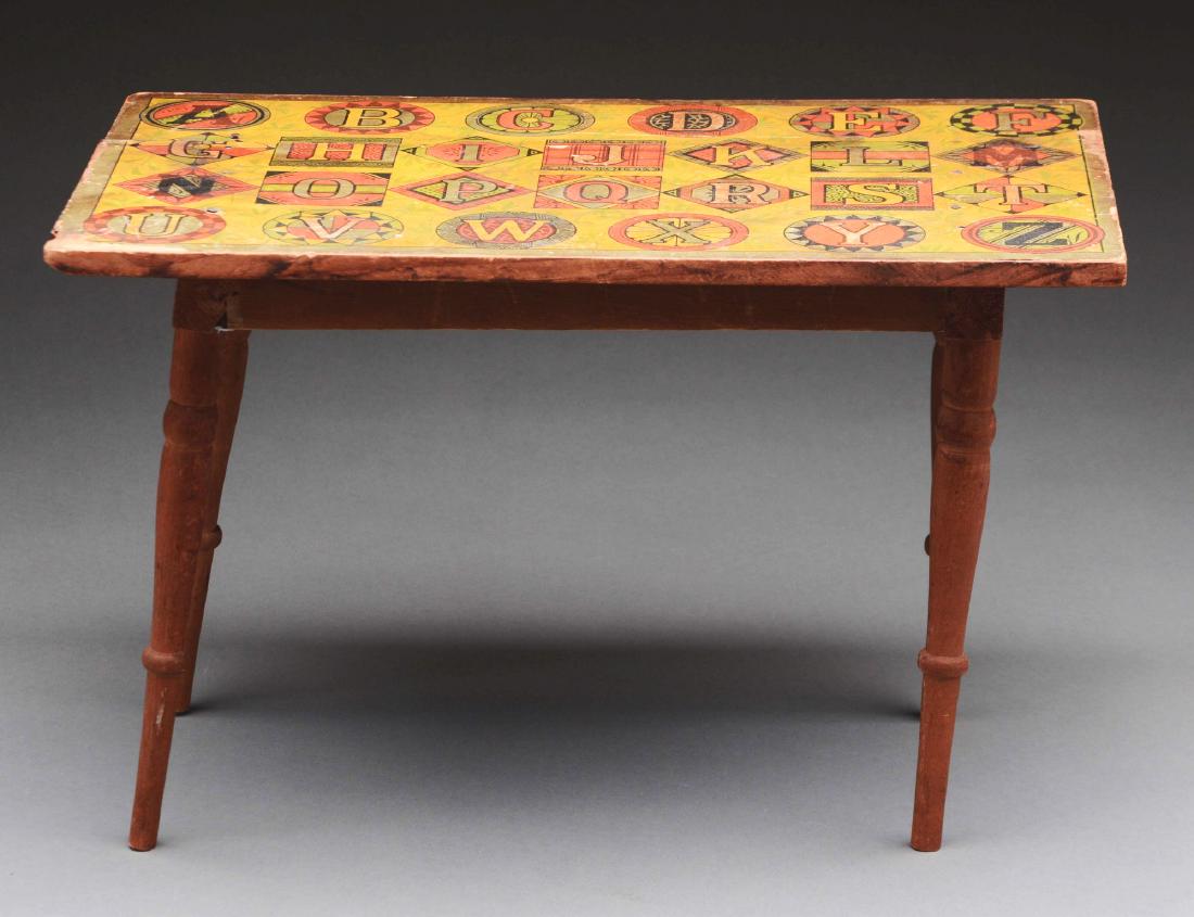 Toy Alphabet Table.: Wood toy table with a lithographed alphabet paper over the top, probably Bliss. There is a crack in the wood top which has caused a split in the paper, some paper loss and some staining.Condition: (Ex