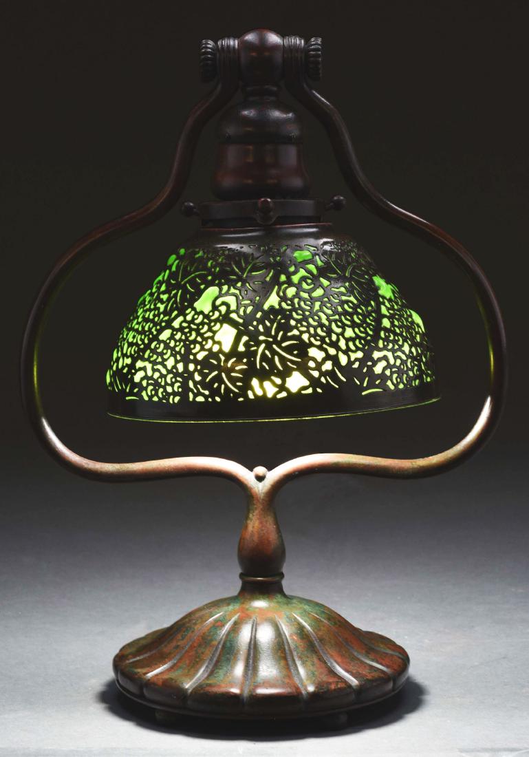 Tiffany Studios Overlay Desk Lamp.: Tiffany Studios desk lamp has a bronze shade in the grapevine pattern. The shade has a green glass liner which is blown out through sections of the grapevine pattern. The bronze is finished in a dark 