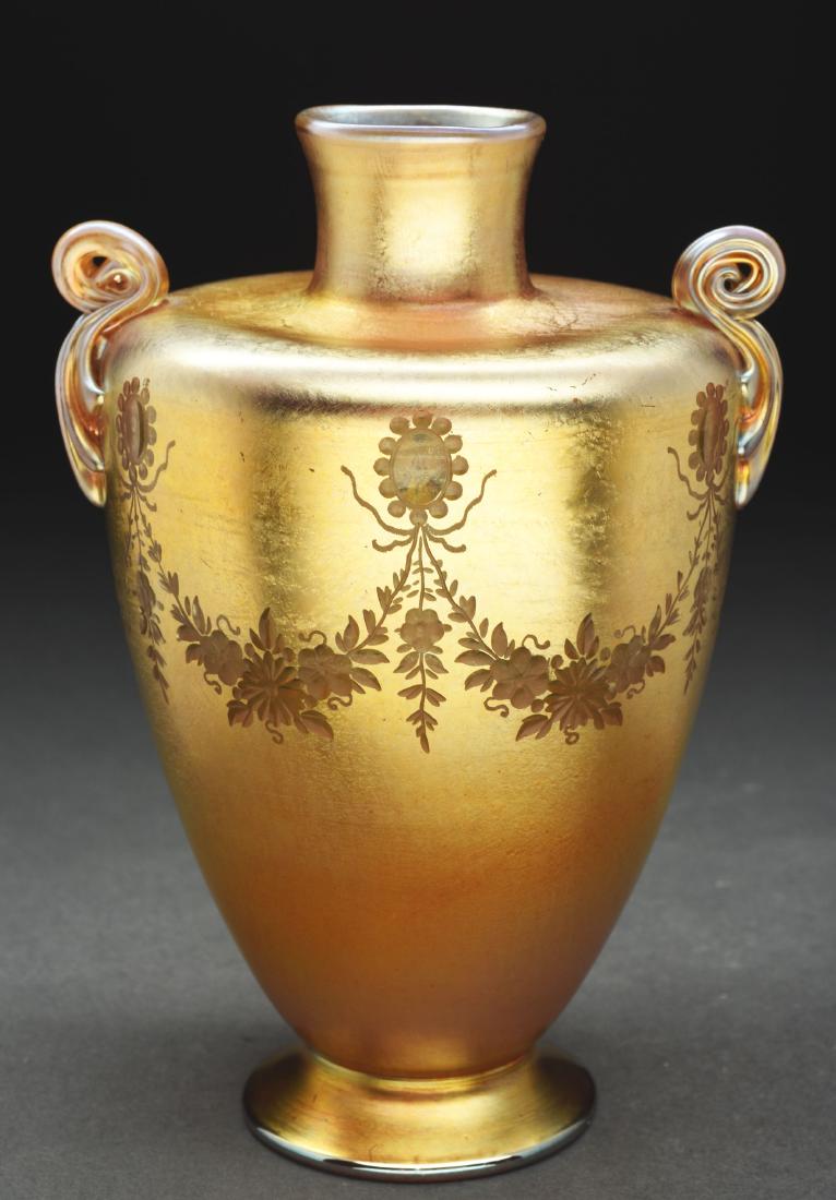 Tiffany Gold Favrile Vase.: Tiffany gold Favrile vase is Itaglio carved with garlands of flowers draping from the shoulder of the vase. The vase is further decorated with two applied and reeded handles. The bright gold iridescen