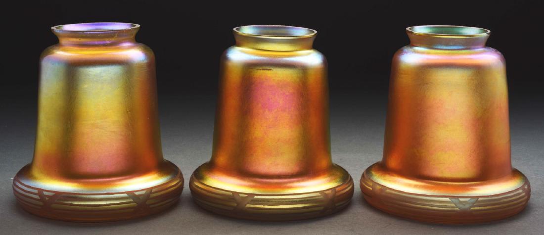 Three Steuben Art Glass Shades.: Set of three Steuben art glass shades in gold aurene. Each shade has a flaring and rounded lip, lip has been carved with a ribbon and cross pattern. The gold iridescent finish shows strong blue highli