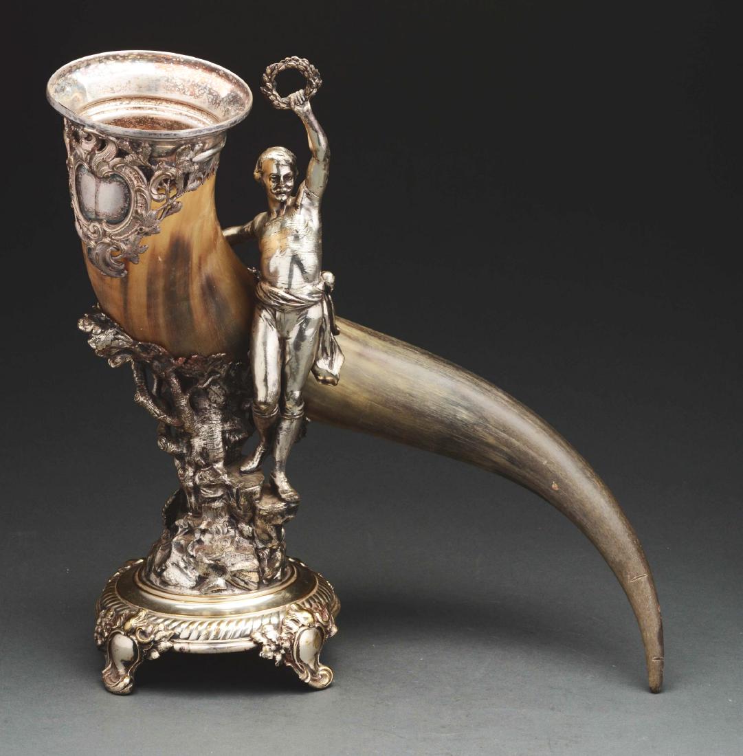 Silver Plate Mounted Horn Trophy.: WMF, the tapering, curving horn held by a plated stand cast with a standing male figure holding a laurel wreath on a base with a tree trunk supporting an oak leaf wreath around the horn, on a domed ba