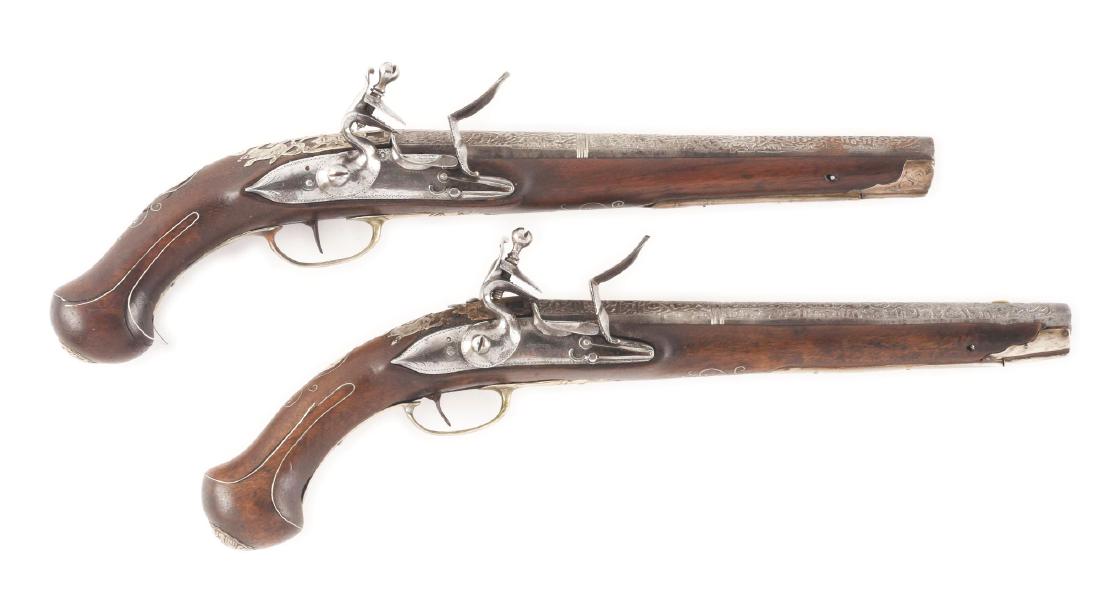 (A) PAIR OF SILVER MOUNTED OTTOMAN HOLSTER PISTOLS: A most interesting pair of Ottoman pistols with 10" Spanish form barrels complete and deeply etched with Islamic calligraphy. The convex locks with roller bearing frizzens. Swan neck cocks with foliat
